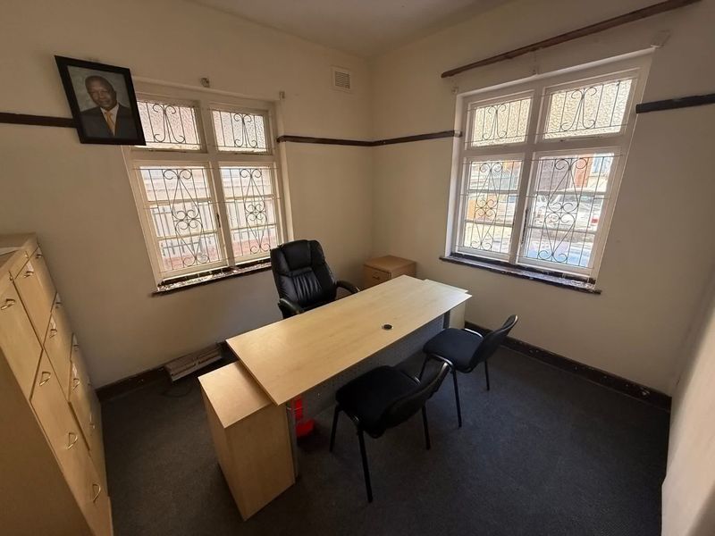 A functional office space featuring dual windows with security bars, carpeted flooring, and built-in storage cabinetry.