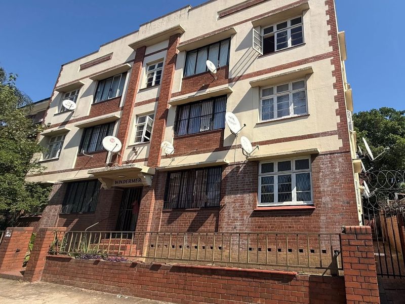 Exterior view of a multi-story apartment building featuring brick and plaster facade, security fencing, and multiple satellite dishes.