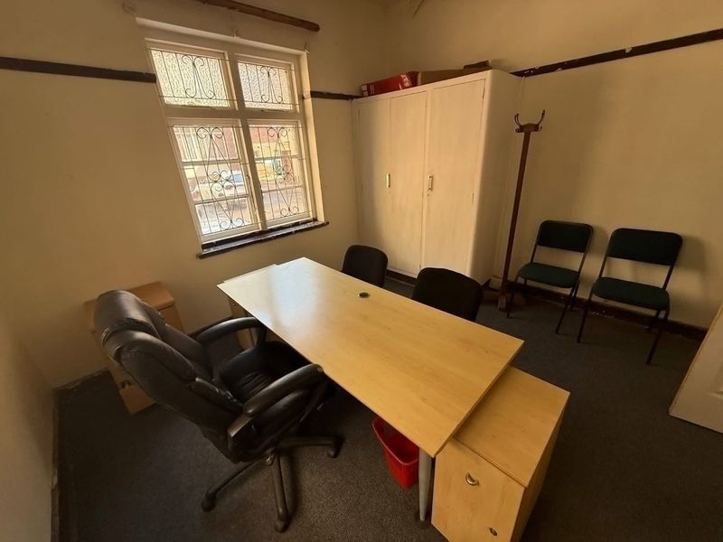 A functional office space featuring a built-in storage cupboard, carpeted flooring, and a window with security bars.
