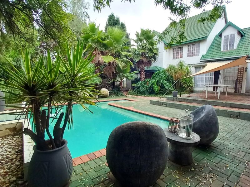 A private outdoor pool area featuring brick paving, a shade sail, and established garden surroundings, adjacent to the main residence.