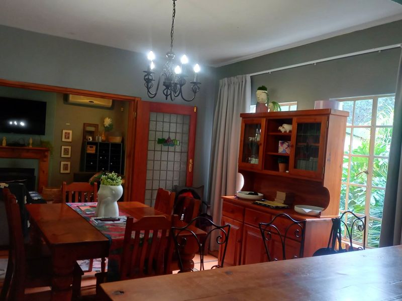 A dining room featuring timber-framed glass doors, a classic chandelier, and large windows providing natural light and garden views.