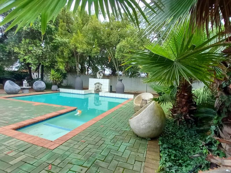 Outdoor swimming pool area featuring brick paving, a built-in water feature, and established garden surroundings.