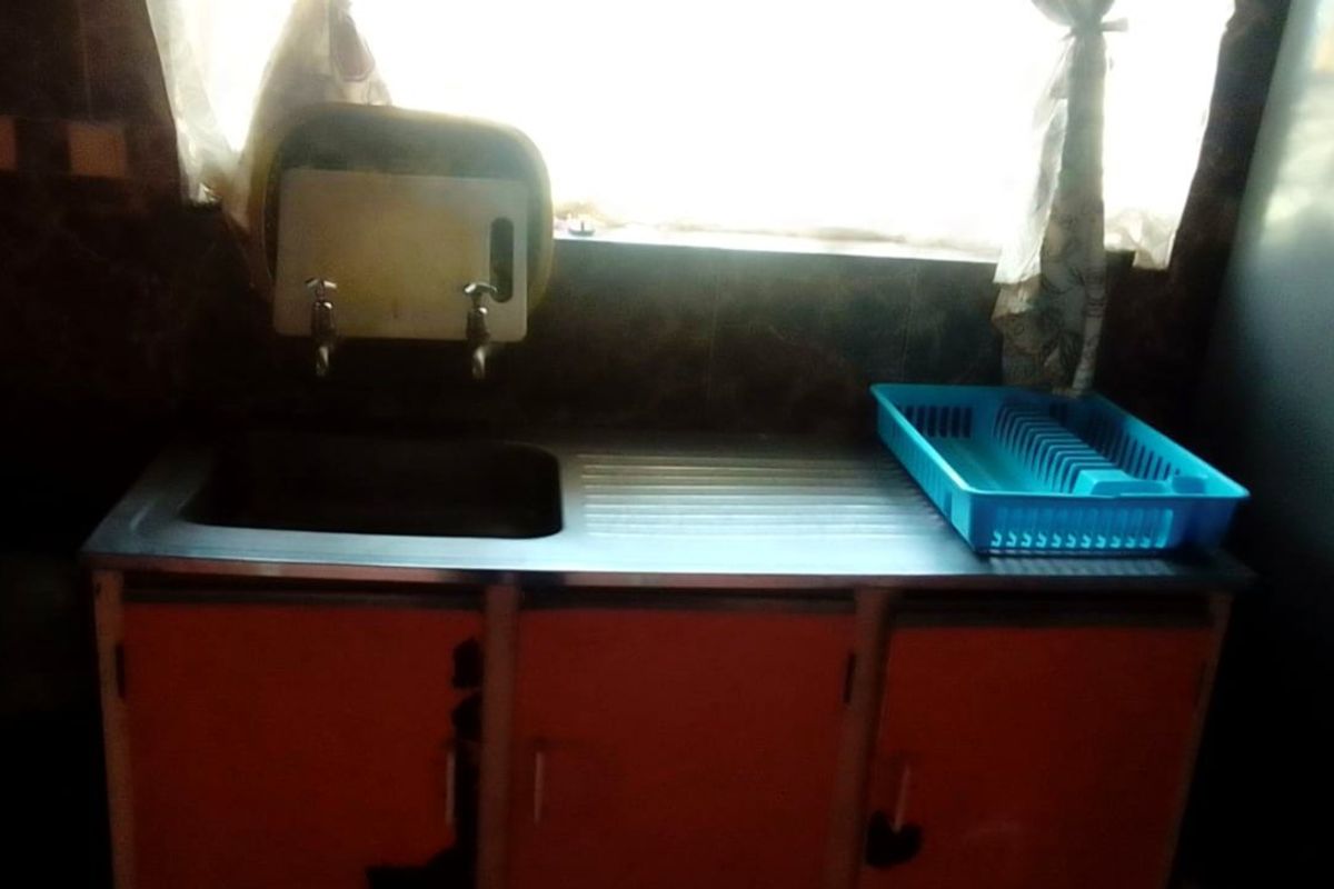 A functional kitchen sink area featuring a stainless steel drop-in sink with integrated drainboard and base cabinetry.