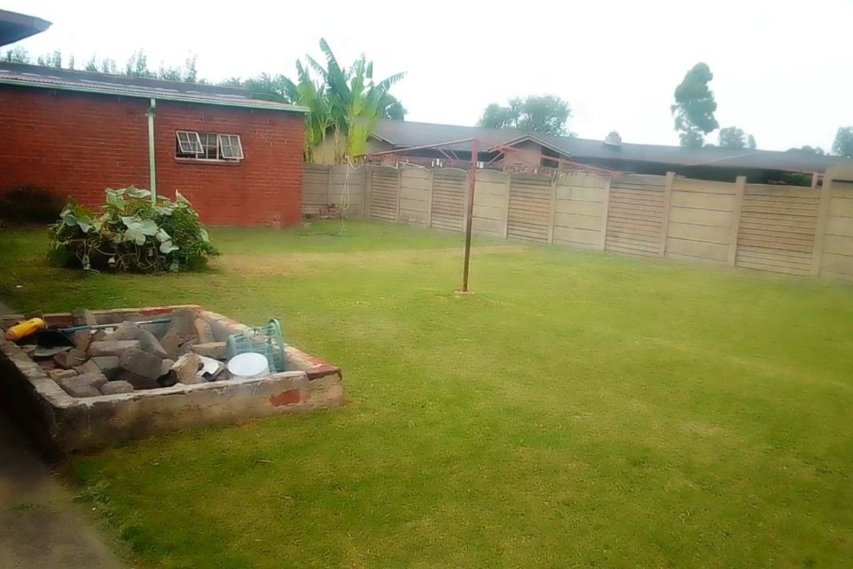 A spacious rear garden featuring a lawn, a brick-built fire pit, and perimeter boundary walling.