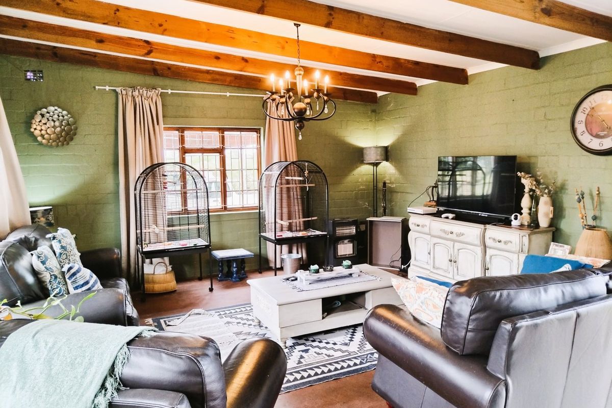 A cozy living room featuring exposed timber ceiling beams, painted brick walls, and a classic wrought iron chandelier, creating a warm and rustic atmosphere.