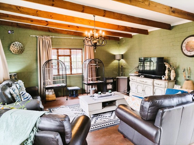 A cozy living room featuring exposed timber ceiling beams, painted brick walls, and a classic wrought iron chandelier, creating a warm and rustic atmosphere.