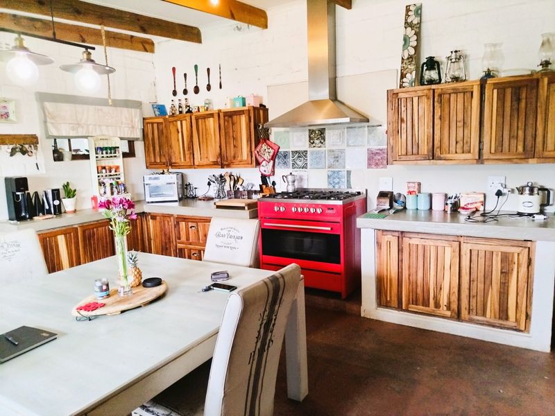 Open-plan kitchen and dining area featuring rustic wooden cabinetry, concrete countertops, a distinctive red range cooker, and exposed timber ceiling beams.