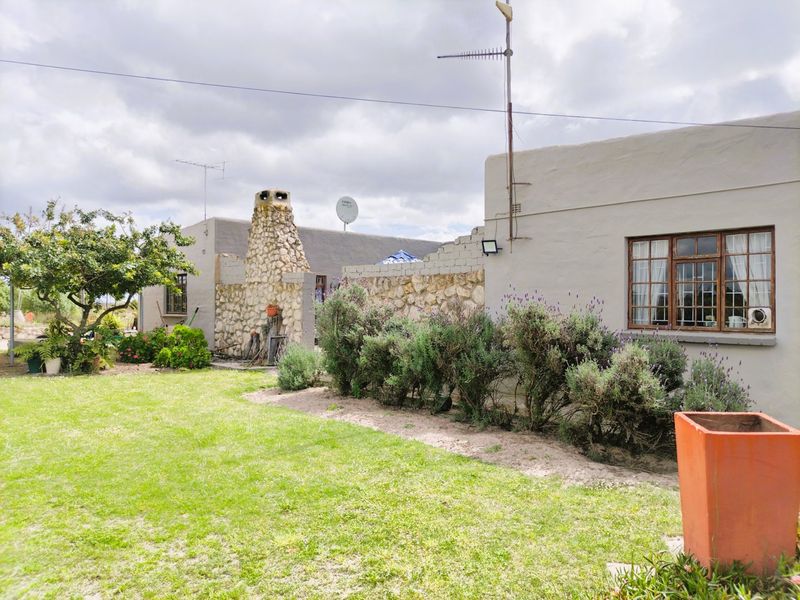 Rear view of the farm property featuring a stone-clad outdoor fireplace, a lawn area, and a stone boundary wall with unfinished masonry sections.