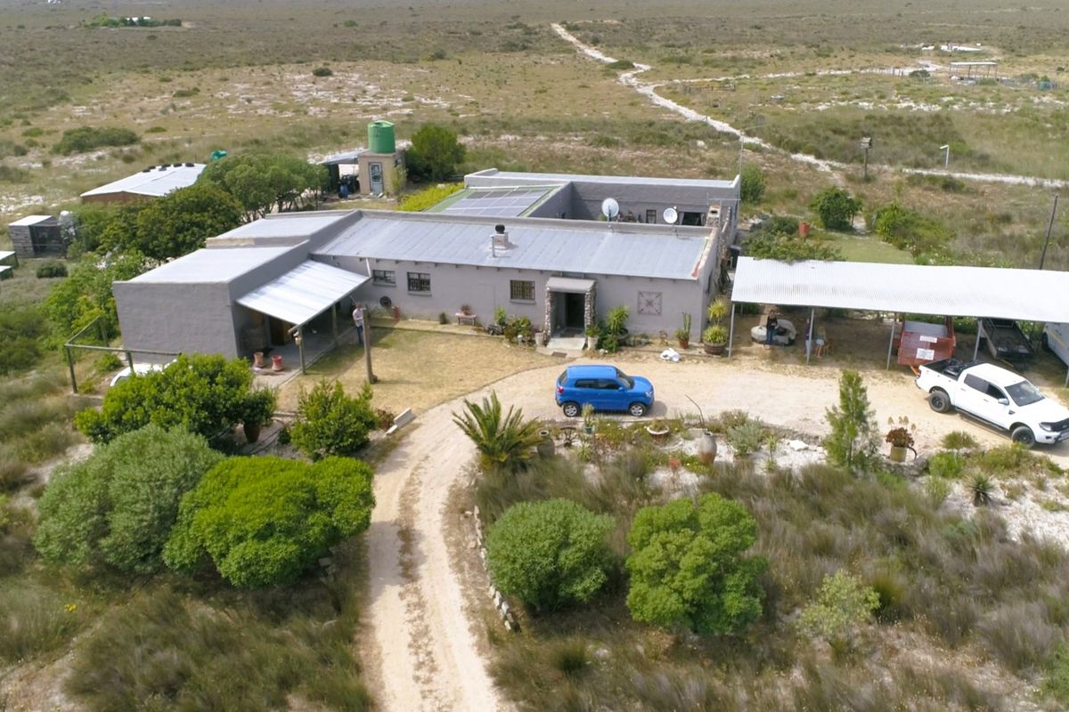 Aerial view of a rural farm property featuring a main dwelling with a metal roof, solar panels, and an attached carport.