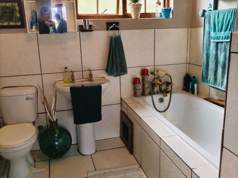 A functional bathroom featuring a pedestal basin, built-in bathtub with brass fixtures, and neutral wall and floor tiling.