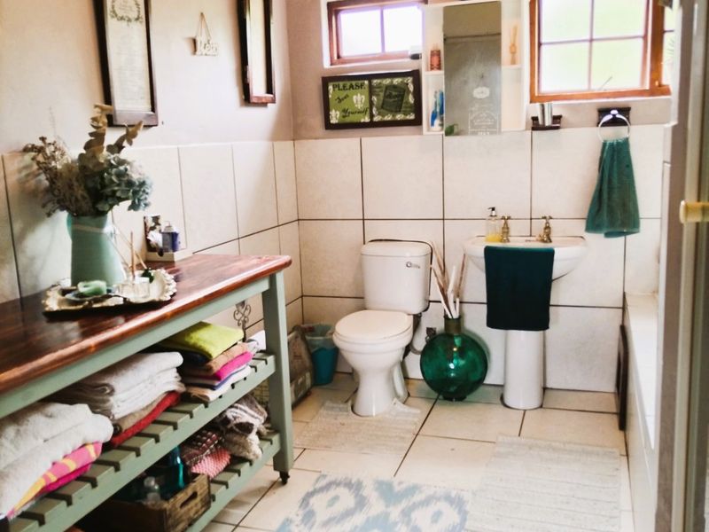 A functional bathroom featuring a pedestal basin, toilet, tiled finishes, and exposed timber ceiling beams, offering a classic farm-style aesthetic.