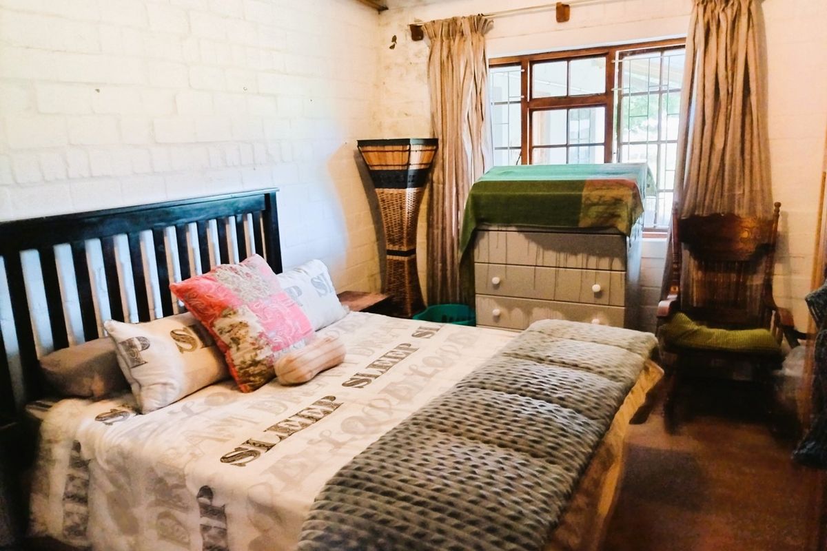 A rustic bedroom featuring exposed brick walls and timber ceiling beams, with a window fitted with security bars.