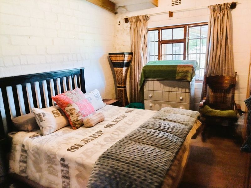 A rustic bedroom featuring exposed brick walls and timber ceiling beams, with a window fitted with security bars.