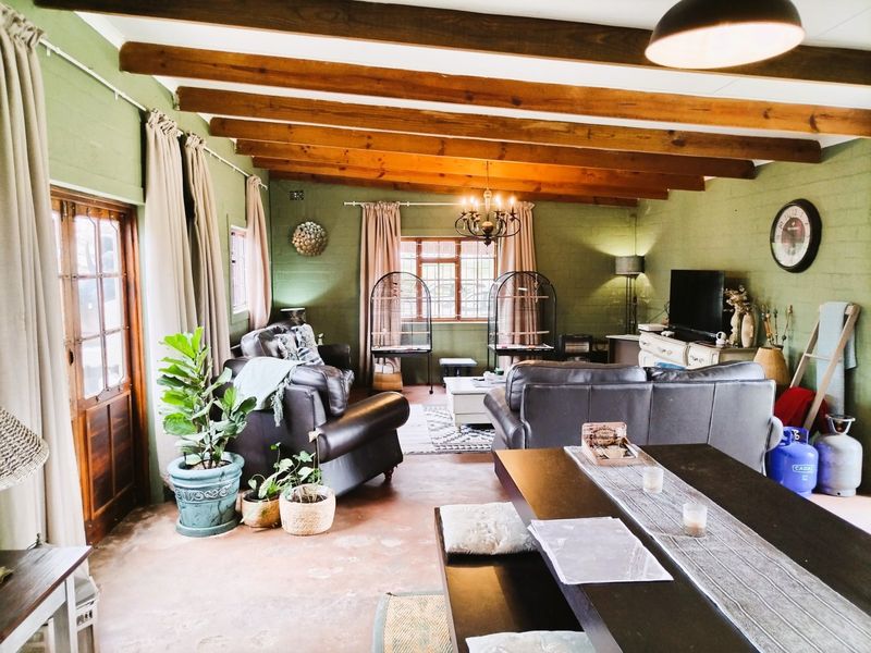 Spacious open-plan living and dining area featuring exposed timber ceiling beams, concrete flooring, and large timber-framed windows providing natural light.
