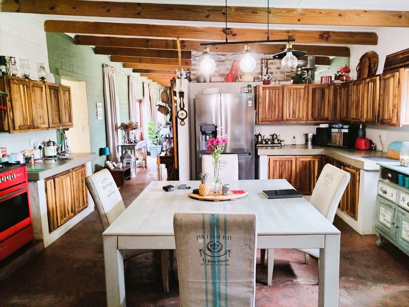 Open plan kitchen and dining area featuring rustic wooden cabinetry, concrete countertops, and exposed timber ceiling beams in a farmhouse style setting.