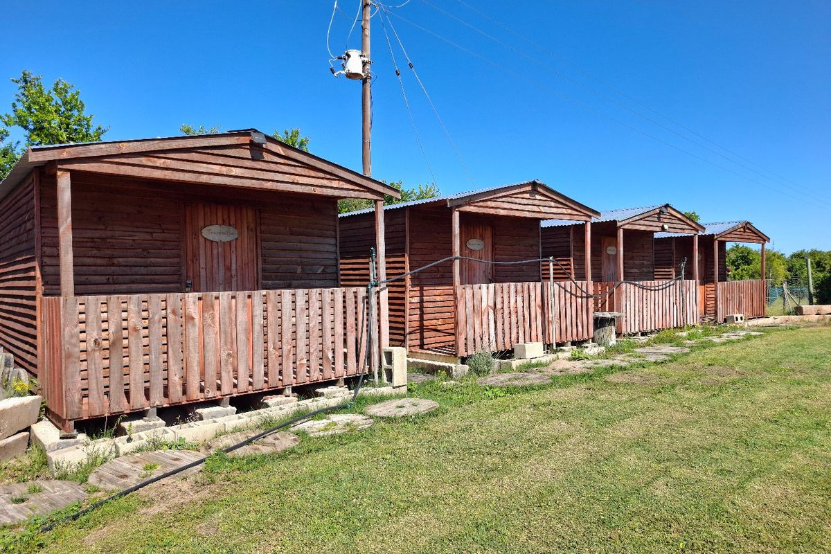 A row of rustic timber cabins featuring covered porches and simple construction, situated on a grassy farm plot.