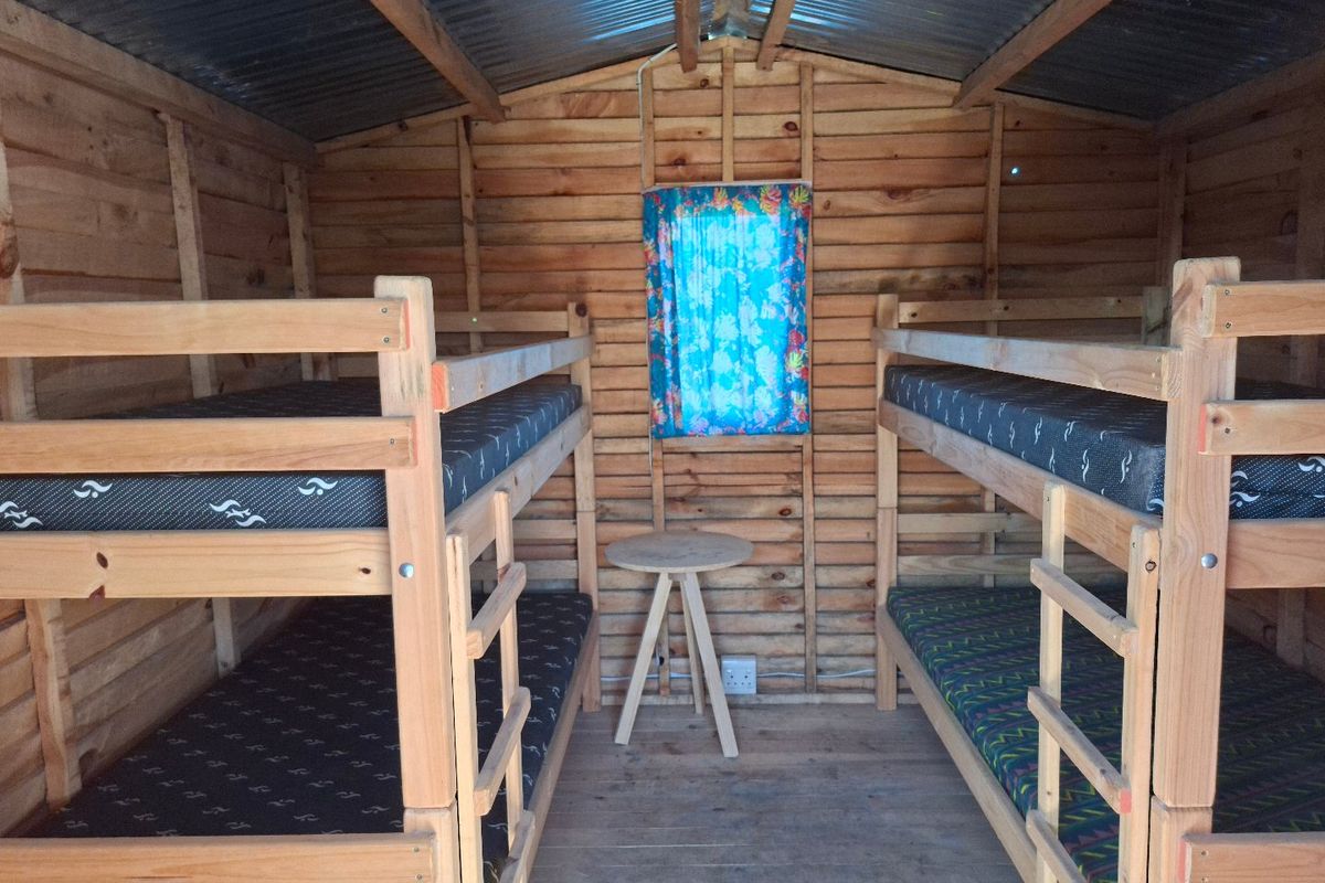 A rustic timber-clad bedroom featuring a corrugated metal roof and wooden flooring, currently configured with bunk beds.