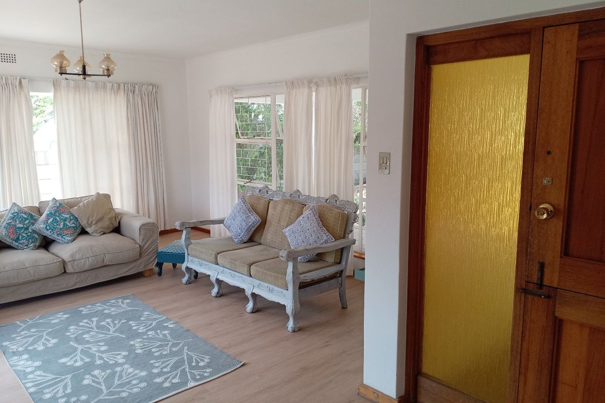 A bright living room featuring light-toned laminate flooring, large steel casement windows, and a classic timber entrance door with a textured glass insert.