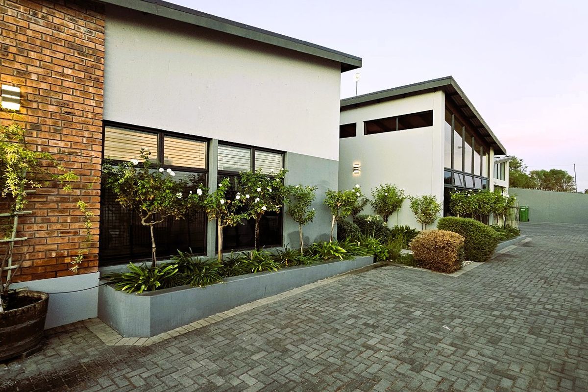 A well-maintained rear exterior view featuring a paved driveway, modern brick and rendered facade, and integrated planter boxes.