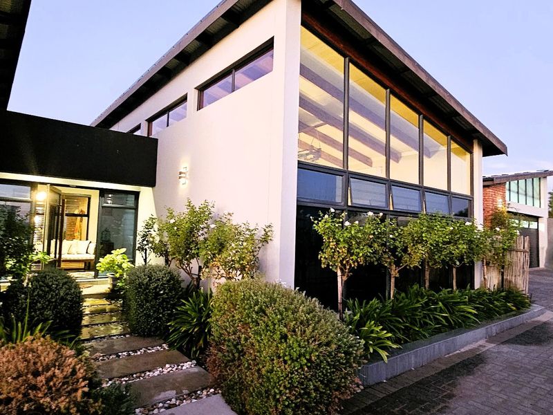 Modern architectural front facade featuring a striking pitched roof, expansive glass windows, paved driveway, and manicured garden landscaping.