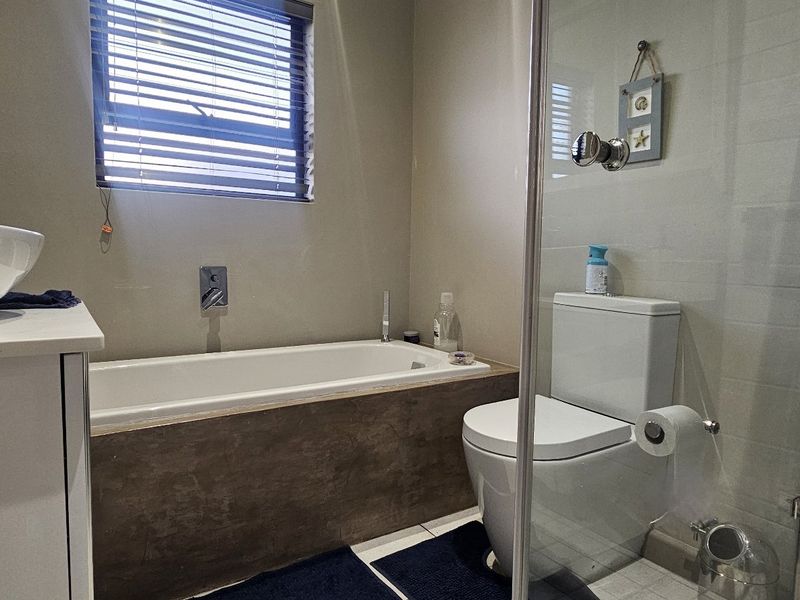 Modern bathroom featuring a vessel sink, built-in bathtub, wall-mounted faucet, and a glass-enclosed shower area with contemporary tiled finishes.