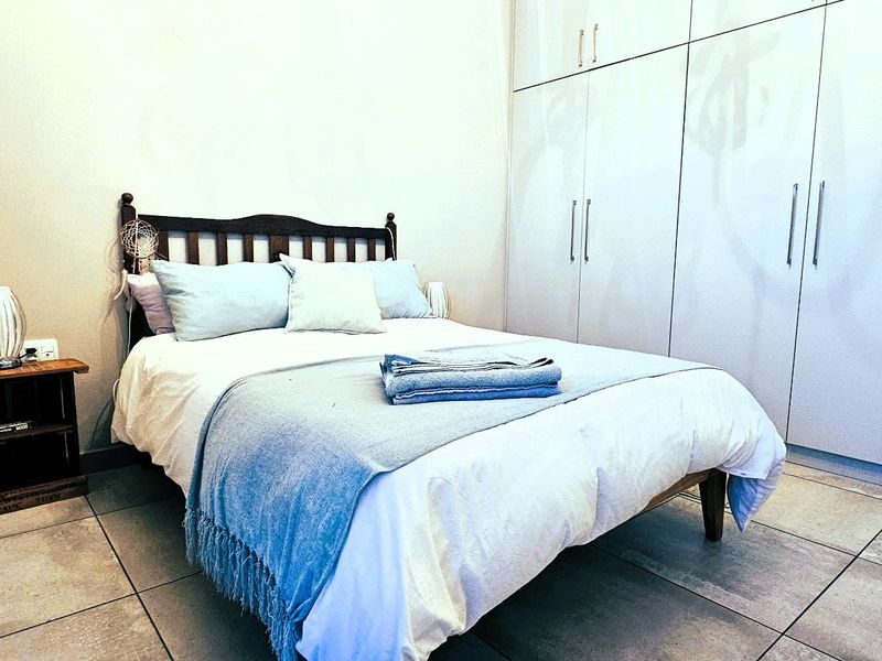 A well-maintained bedroom featuring neutral tiled flooring and extensive floor-to-ceiling built-in cupboards for ample storage.