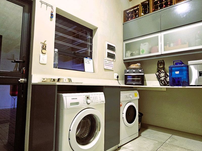 A functional laundry room featuring built-in cabinetry, overhead storage, tiled flooring, and direct access to an outdoor area.