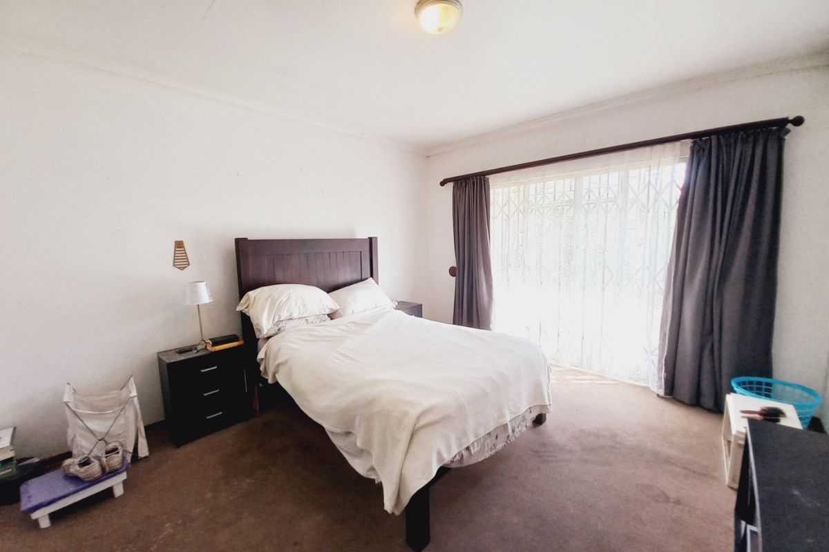 A standard bedroom featuring carpeted flooring, a ceiling light fixture, and a sliding door with a security gate and curtain rod.