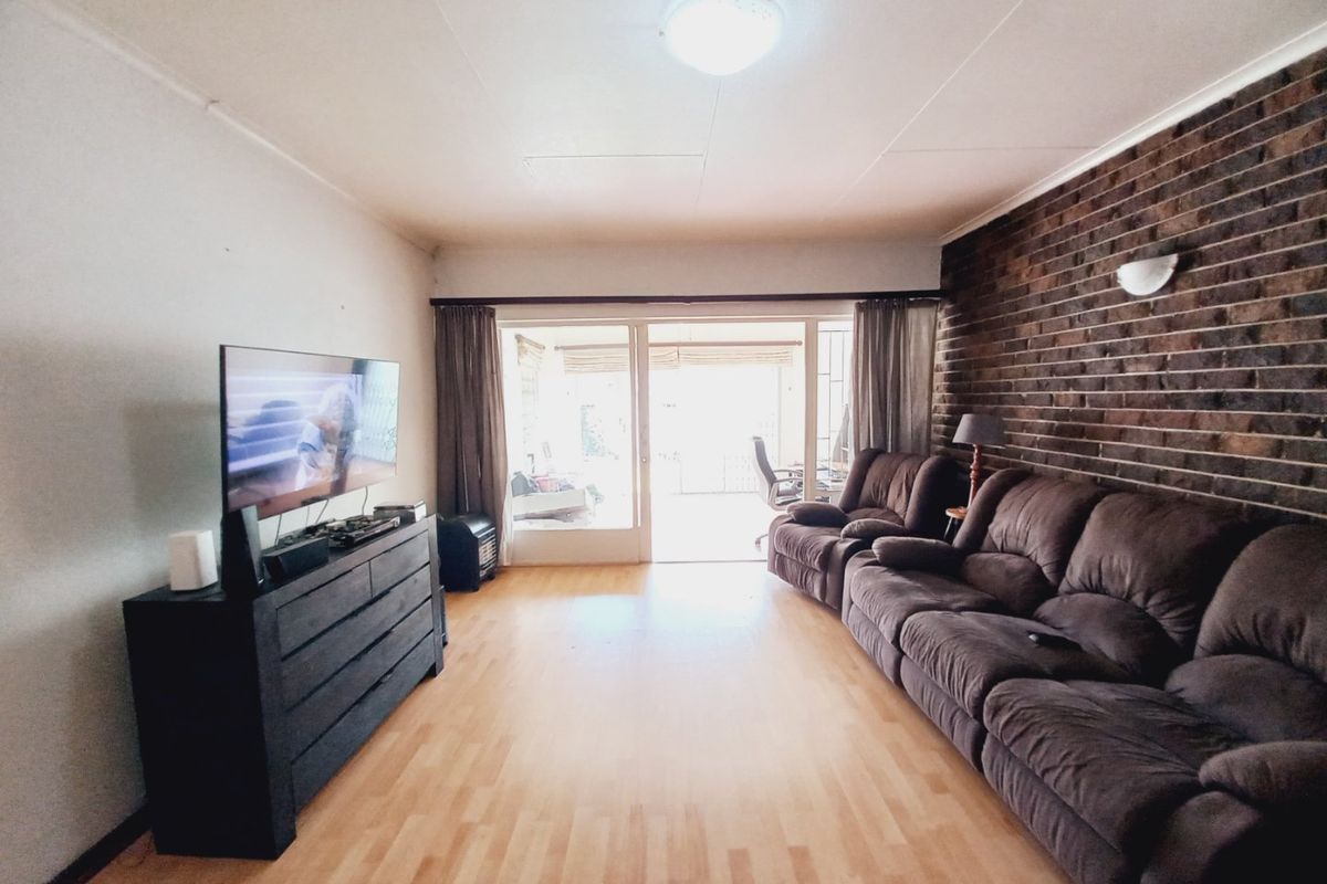 A living room featuring a prominent exposed brick wall, laminate flooring, and a sliding glass door providing access to the outdoor area.