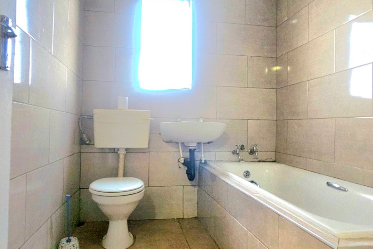 A functional bathroom featuring a bathtub, wall-mounted basin, and toilet, finished with neutral ceramic wall and floor tiles.
