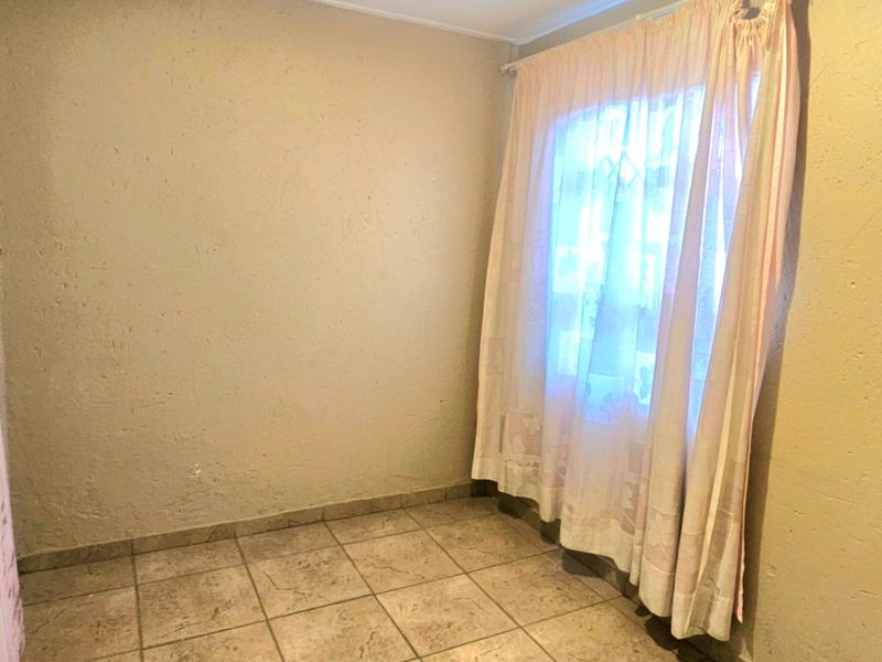 An empty bedroom featuring tiled flooring, neutral wall finishes, and a window with a curtain rail.