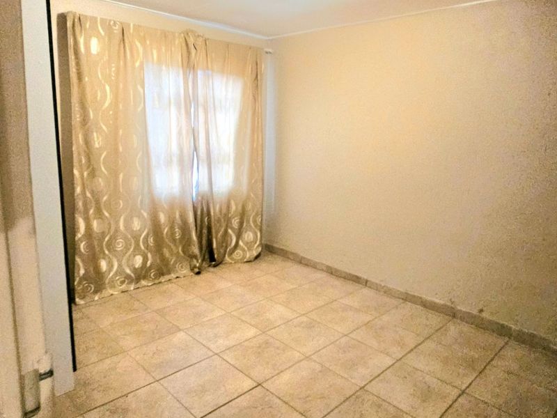 A vacant bedroom featuring neutral tiled flooring and a simple ceiling light fixture, offering a blank canvas for potential interior updates.