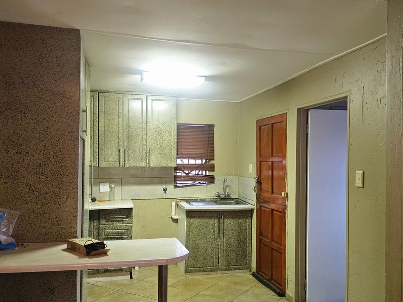 A functional kitchen featuring built-in cabinetry, tiled backsplash, and tiled flooring, offering a practical layout with direct access to adjacent rooms.