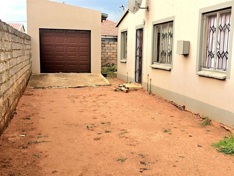 Rear exterior view showing a detached garage, security gates on windows, and an unpaved yard area with a concrete driveway section.