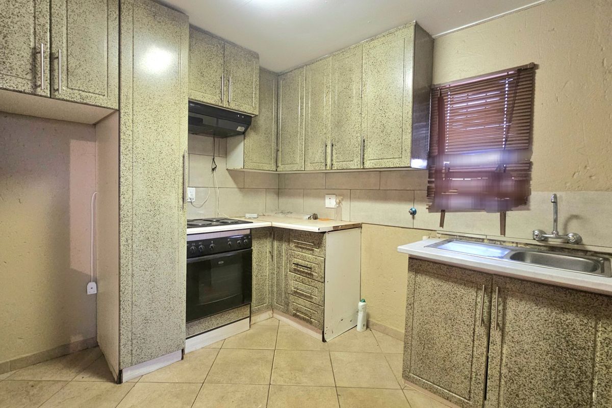 A functional kitchen featuring built-in cabinetry, an electric stove with extractor fan, and a double sink, offering a practical layout for renovation.