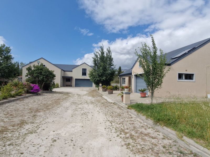 Front view of a residential property featuring a gravel driveway, double garages, and established garden areas with a paved walkway.