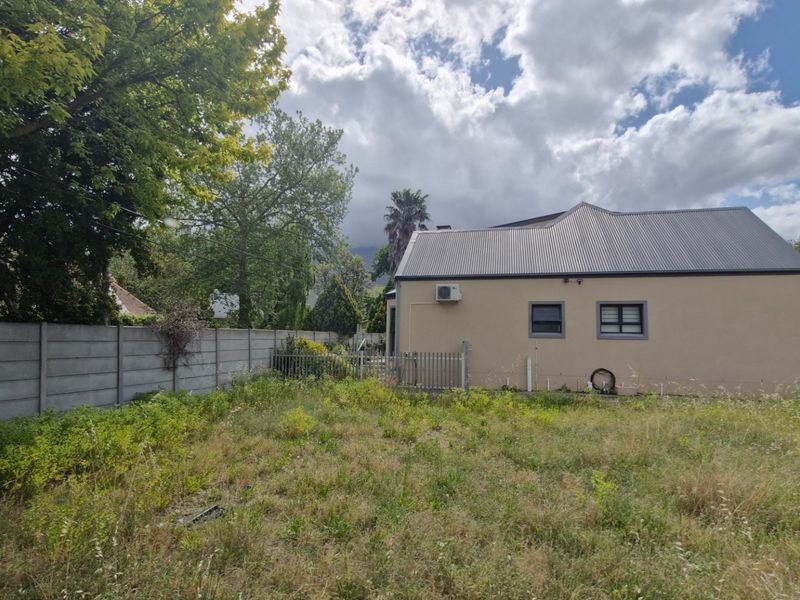 Rear view of the residential property featuring a large, overgrown garden area, precast boundary wall, and metal roof structure.