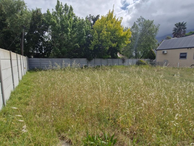 A vacant residential plot featuring an overgrown grass area enclosed by a precast concrete boundary wall.