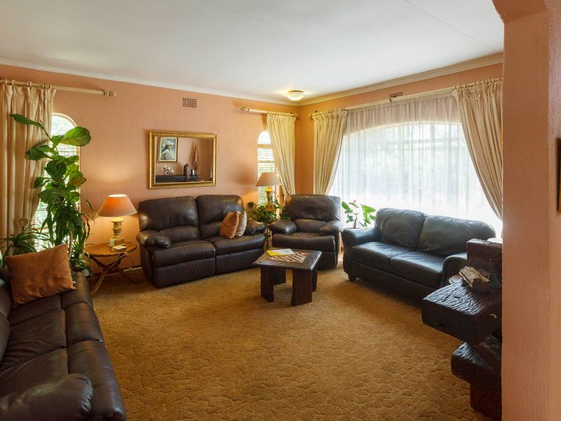 A spacious living room featuring large arched windows, textured walls, and carpeted flooring, offering a comfortable and traditional layout.
