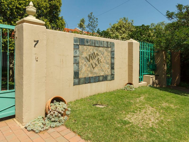 Front boundary wall featuring a decorative tile inlay, metal security gate, and paved driveway entrance.