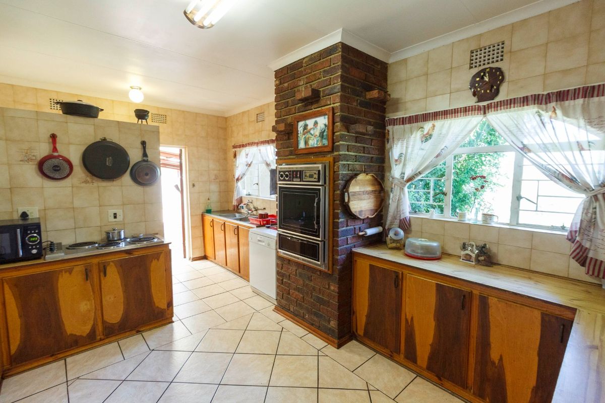 A dated kitchen featuring a prominent brick chimney breast, tiled splashbacks, fitted wooden cabinetry, and a built-in oven with a hob.