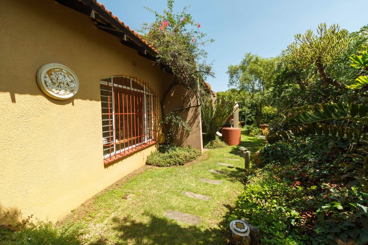 A well-maintained rear garden area featuring a stone pathway, established greenery, and a building facade with security bars on the windows.