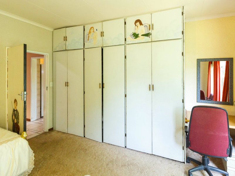 A bedroom featuring extensive built-in cupboards with overhead storage and carpeted flooring, offering potential for modernization and updated finishes.