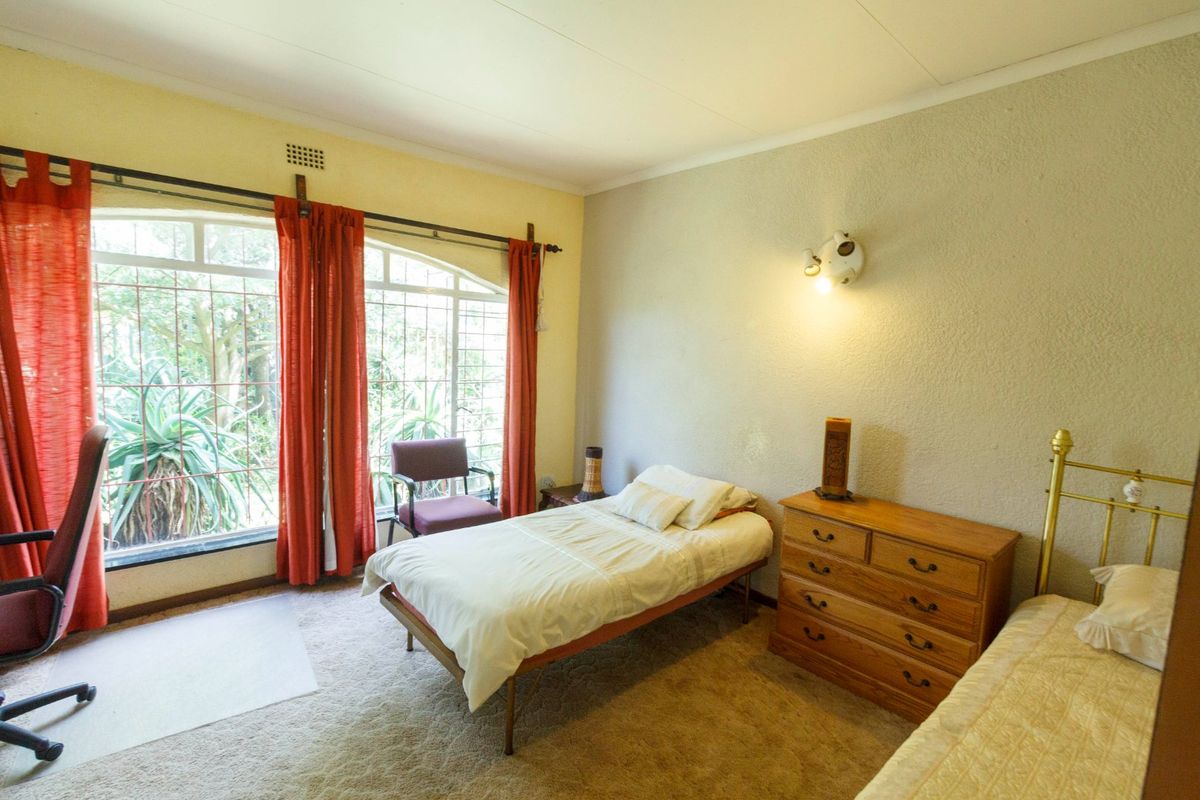 A bedroom featuring a large arched window with security bars, carpeted flooring, and a wall-mounted light fixture.