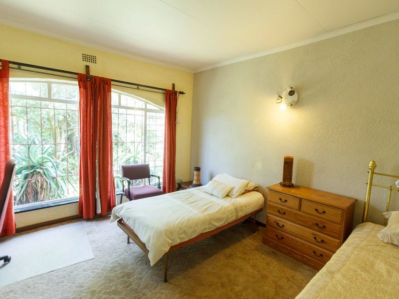 A bedroom featuring a large arched window with security bars, carpeted flooring, and a wall-mounted light fixture.