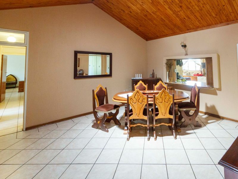 Dining room featuring a vaulted timber ceiling, tiled flooring, and a convenient serving hatch connecting to the kitchen area.