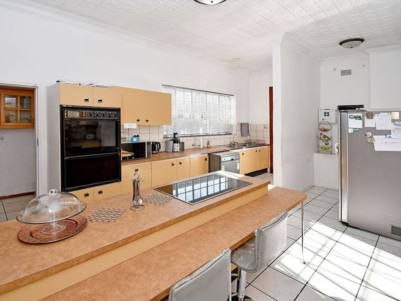 Spacious kitchen featuring a central island with integrated hob, built-in oven, ample cabinetry, and tiled flooring, offering a functional layout with potential for modernization.