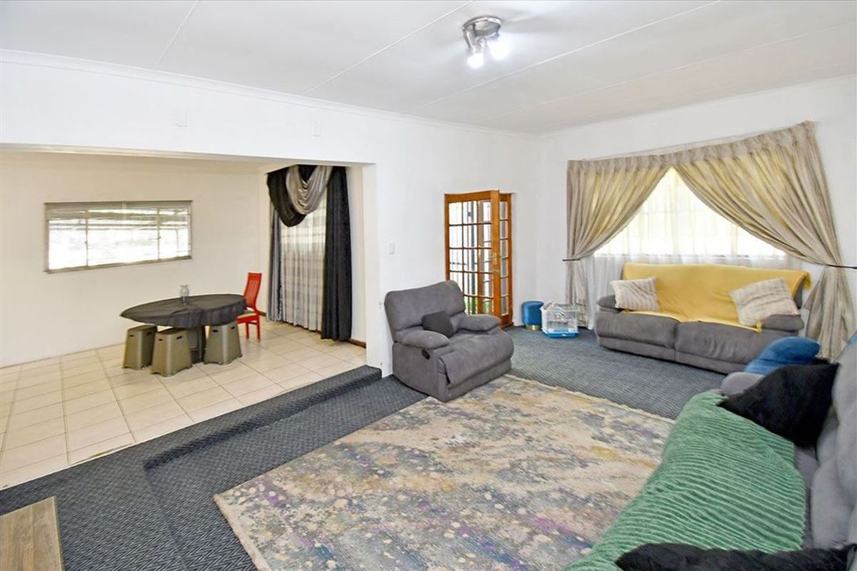Open-plan living and dining area featuring a combination of carpeted and tiled flooring, with a timber-framed glass door and neutral wall finishes.