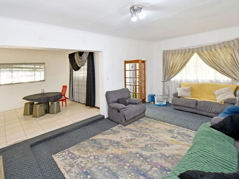 Open-plan living and dining area featuring a combination of carpeted and tiled flooring, with a timber-framed glass door and neutral wall finishes.