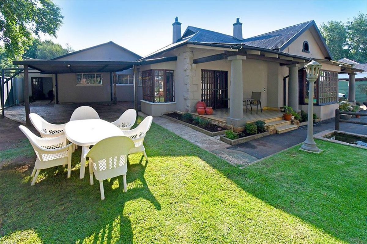 Rear view of the property featuring a covered patio, attached carport, and a landscaped garden with a small pond.
